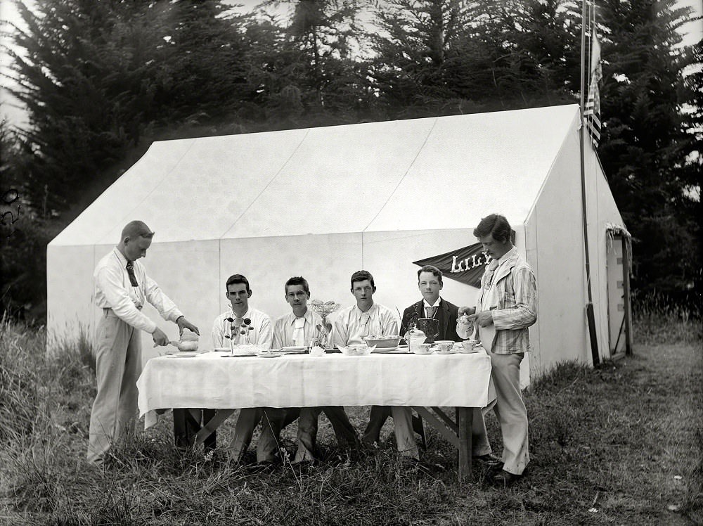 #28 Young men in formal wear at table ready to have a meal, next to tent ‘Lily’ at camp site, probably in Sumner, Christchurch, New Zealand, 1910