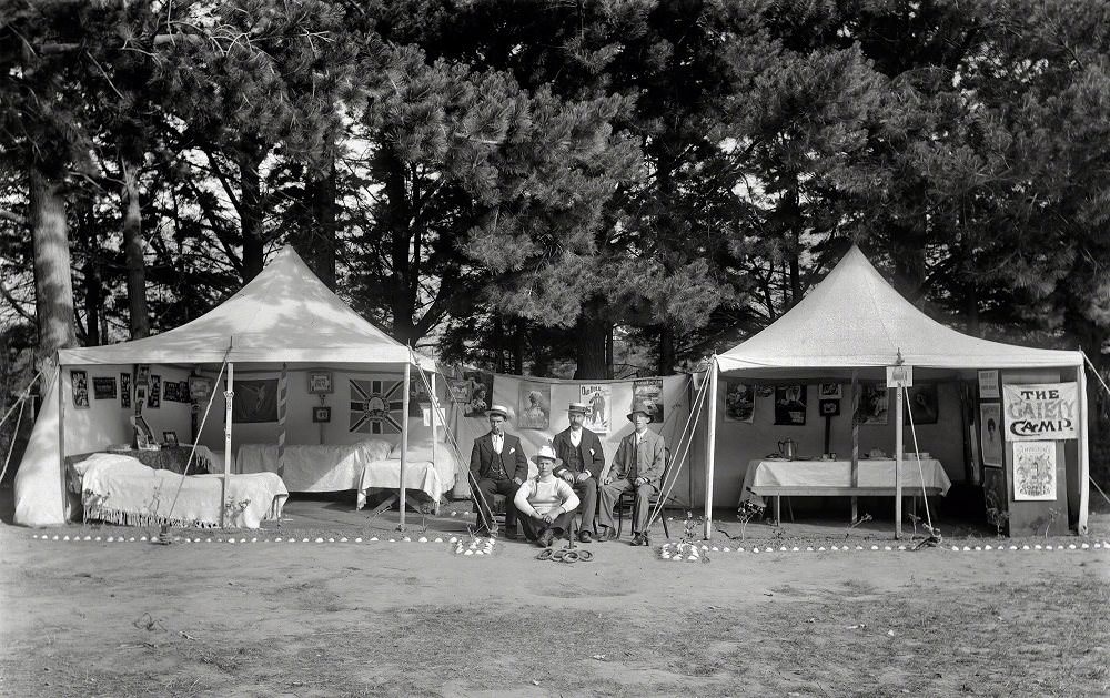 #30 Unidentified men sitting between two open tents with beds, tables, pictures, flags and posters on the walls, New Zealand, 1910
