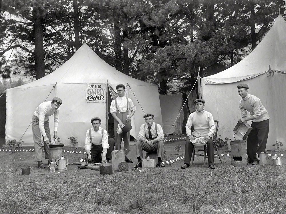 #32 Group men outside a tent with a sign reading ‘The Gaiety Camp,’ showing each man performing domestic duties, Christchurch district, New Zealand circa 1910