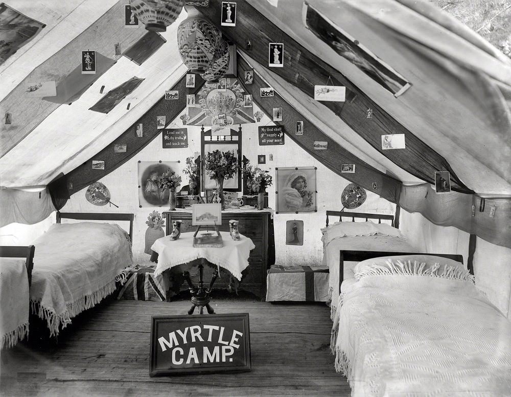 #58 Interior of large tent decorated with posters and picture postcards, with tallboy and mirror, trunks with flags, lamps and ‘Myrtle Camp’ sign, Christchurch, New Zealand circa 1905
