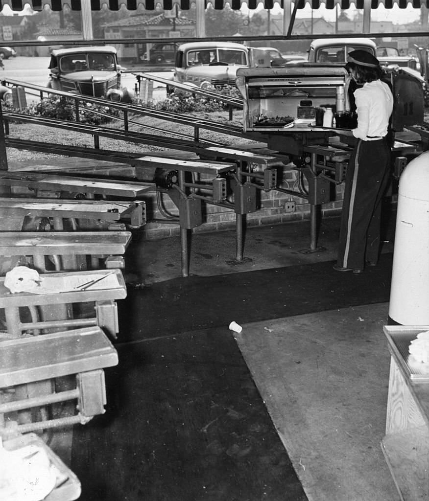 #13 A woman loads a box, which will deliver food to a waiting car at a drive-in restaurant in Hollywood, 1955