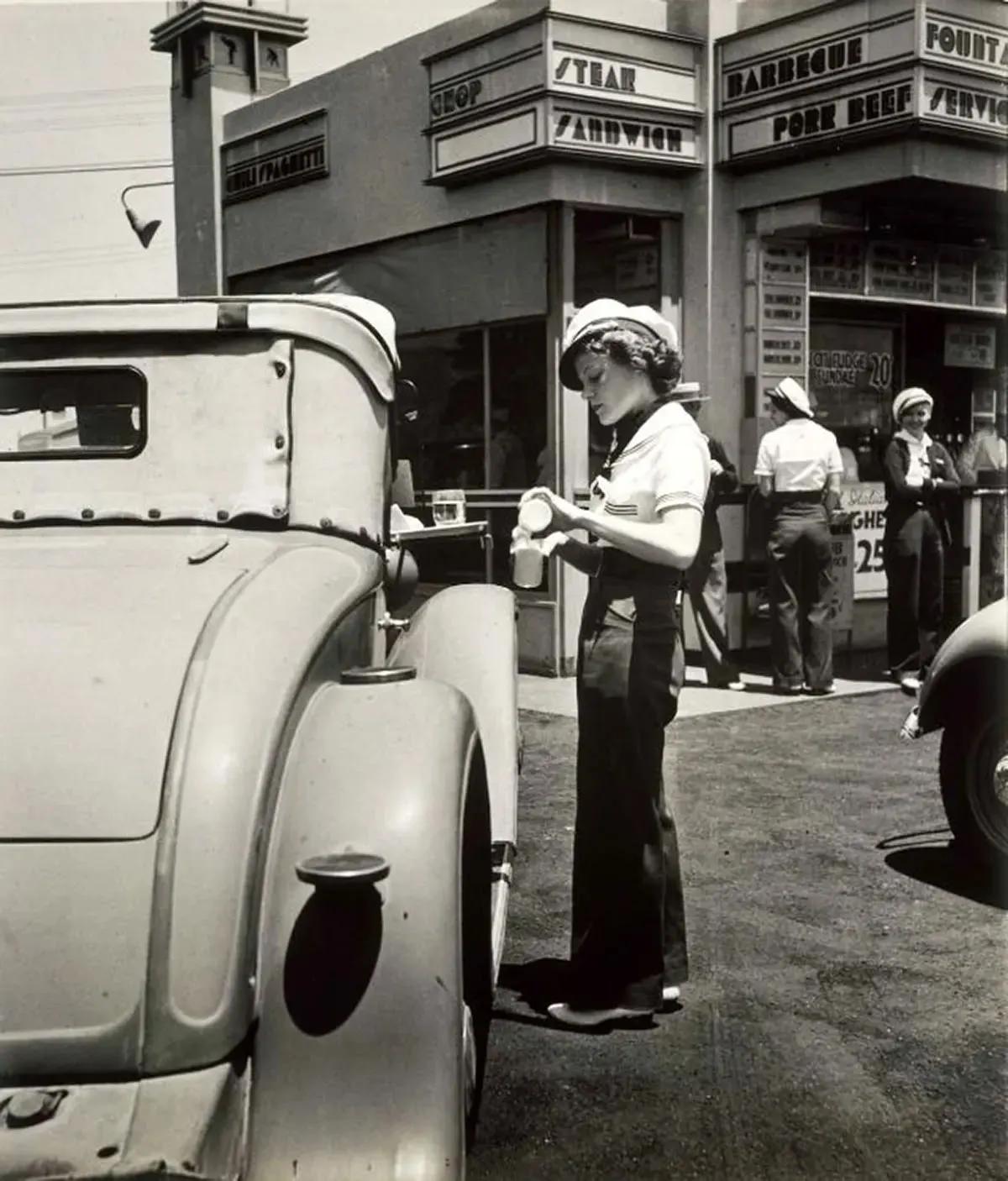 #39 A carhop pouring milk from a bottle into a glass, at McDonnell’s Drive-In. 1930s.