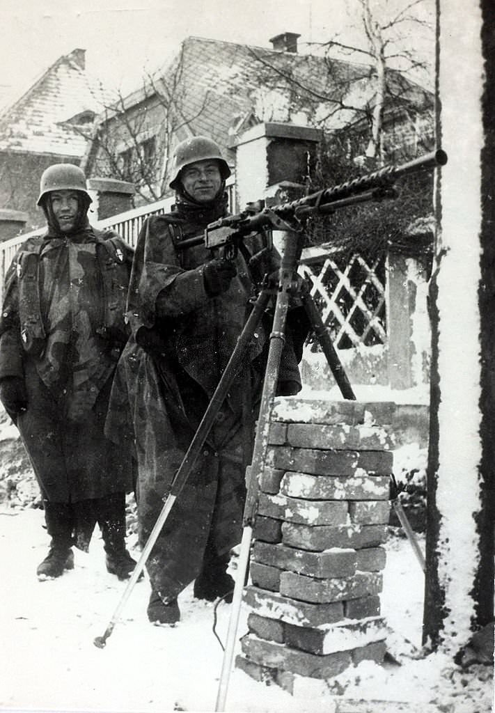 #105 German machine gunners muffled to the ears against the severe cold stand ready for action in a Prague street.