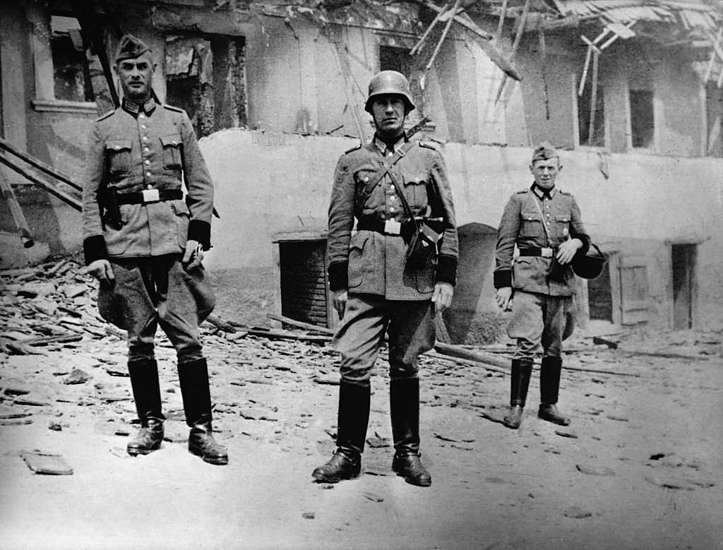 #20 German soldiers pose in front of the burnt out shell of a farmhouse in Lidice.