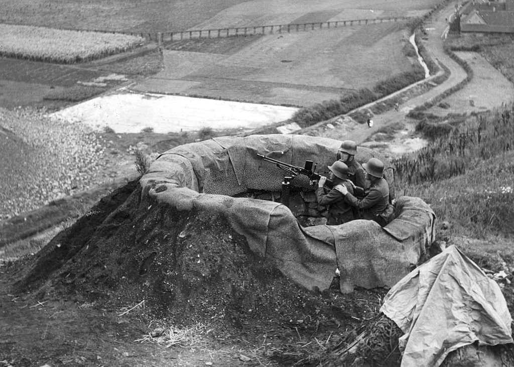 #62 Three German soldiers sit behind an anti-aircraft machine in a camouflaged post overlooking the Sudetenland countryside, Czechoslovakia, World War II.