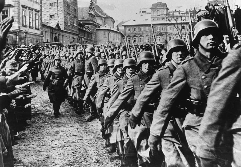 #63 Steel helmeted German troops marching into Prague during the invasion of Czechoslovakia. By-standers are giving them a German salute.