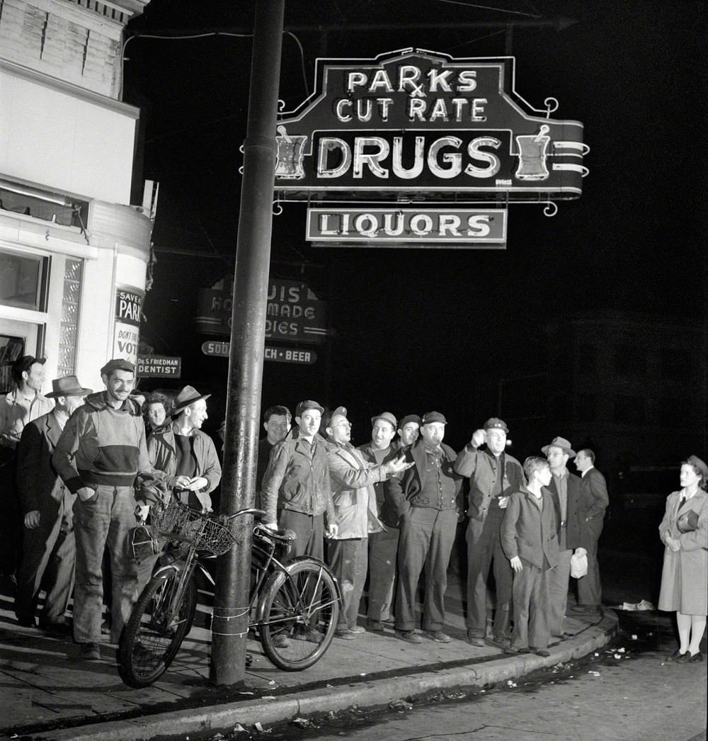 #64 Workers waiting on a street corner to be picked up by car pools around midnight, Baltimore, 1943