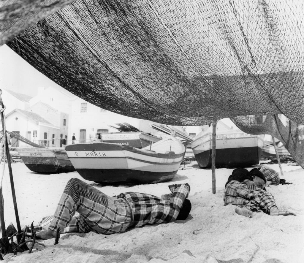 #1 Portugeuse fishermen in traditional checks having a siesta underneath their nets on the beach at Nazare, 80 miles north of Lisbon, 1958