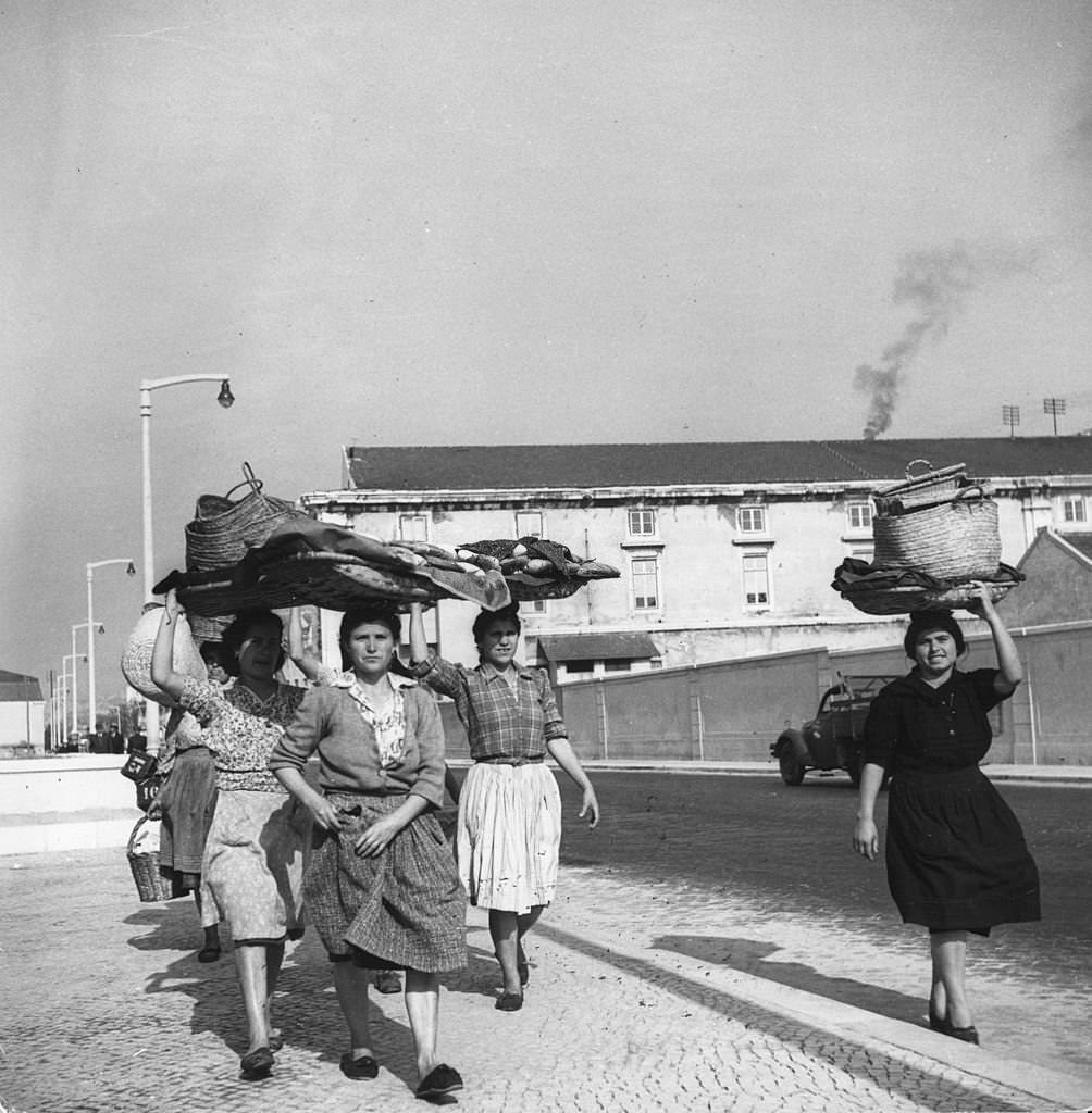 #11 Portuguese fisherwomen, known as ‘varinas’, walk along the docks on the Tejo River carrying empty baskets which they use to take fish to market, 1955