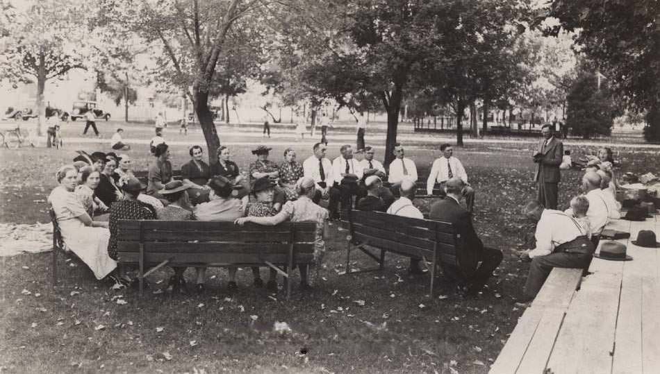 #103 Dr. Reverand Clarence Sands, First Baptist Church in San Jose in front of a group of people sitting on park benches, 1945