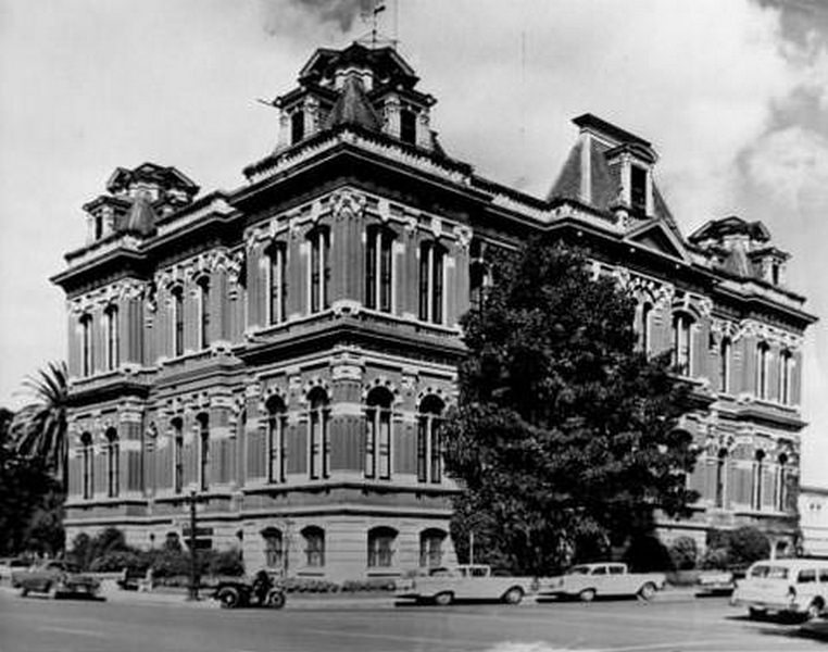 #71 Exterior view of San Jose City Hall with cars and a motorcycle parked alongside it, 1957