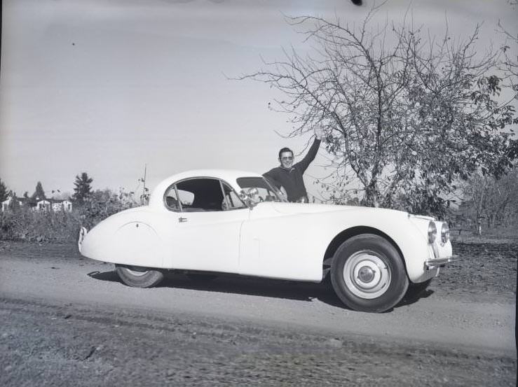 #52 BIll Emerson posing with his jaguar sportscar on a country road, 1954