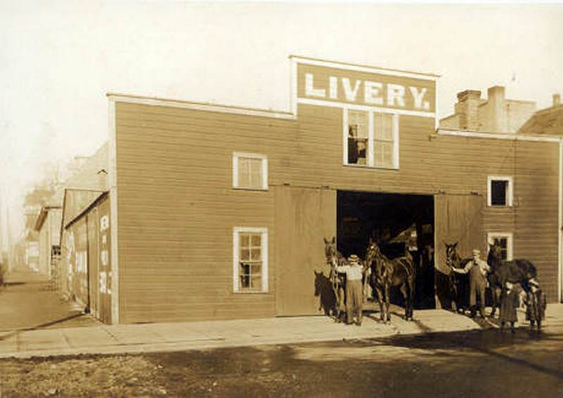 #51 John Crass (in white shirt) walking out horses with a helper at a livery stable located at 214 West 4th Street in Vancouver, 1900s