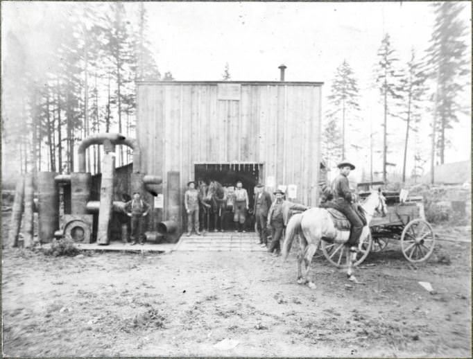 #54 Men stand before a blacksmiths shop with pipes and conduits off to the side, 1904
