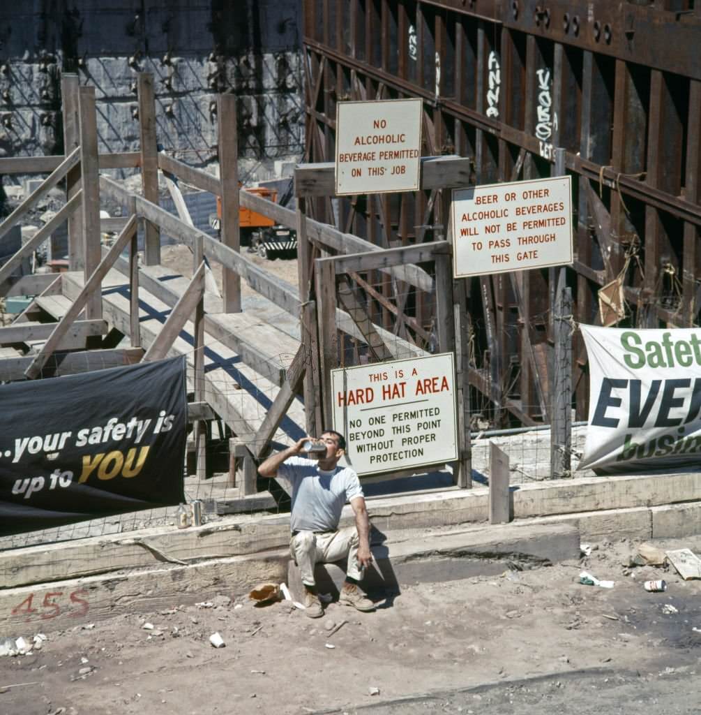 #41 A construction worker as he drinks from am insulated flask, seated on a curb outside the World Trade Center construction site, 1969
