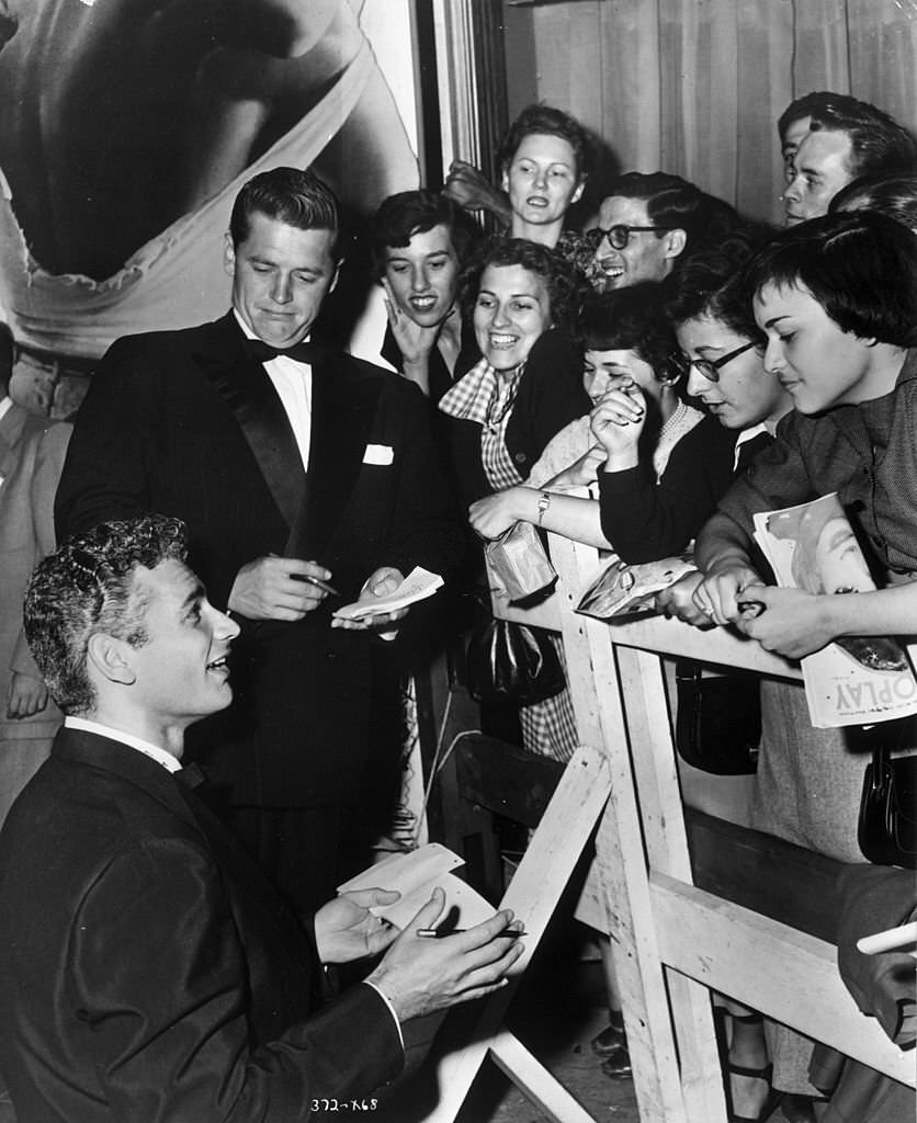 Jeff Chandler (L) and Gordon MacRae sign autographs for smiling fans waiting behind a barrier at the Hollywood premiere of ‘Streetcar Named Desire,’.
