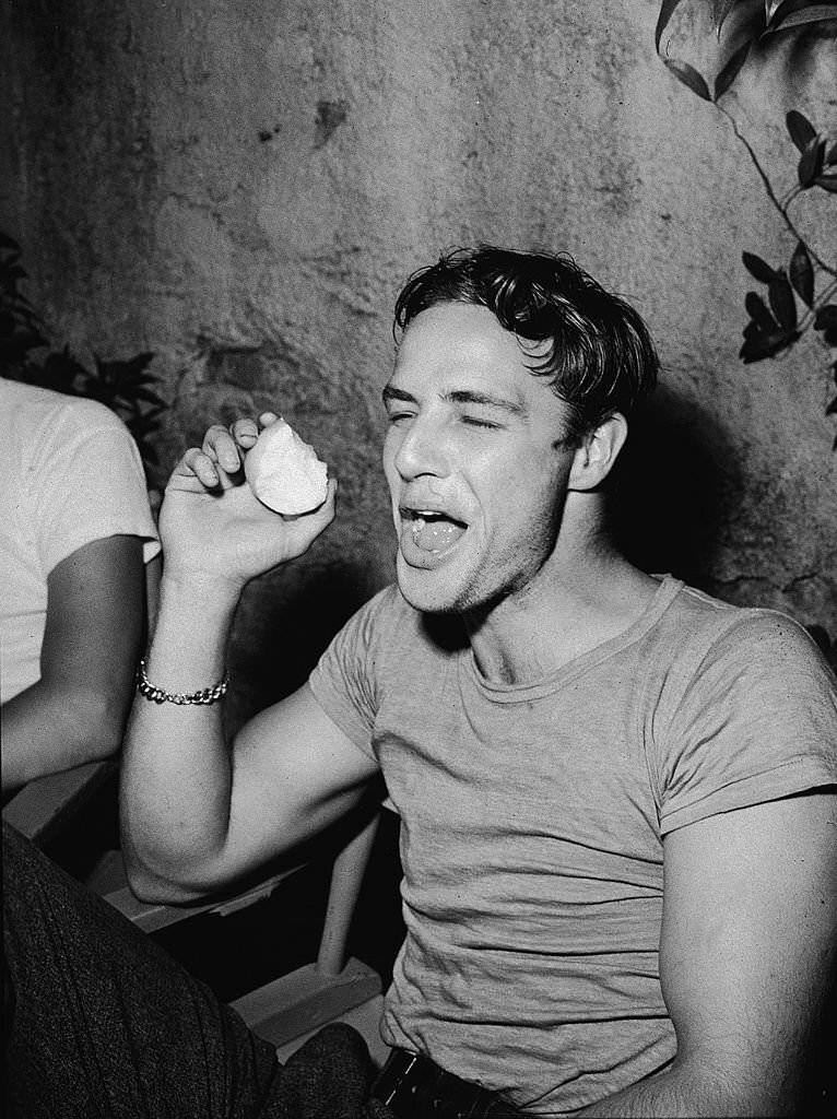 Marlon Brando laughs while eating an apple during a break on the set of the film, ‘A Streetcar Named Desire, 1951
