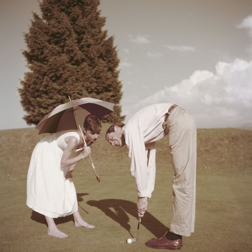 #57 Audrey Hepburn with her husband Mel Ferrer on a golf course at the Bürgenstock resort, Switzerland, 1954.