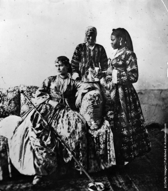 #135 A white lady in crinoline, attended by two women, in a harem in Cairo, 1870