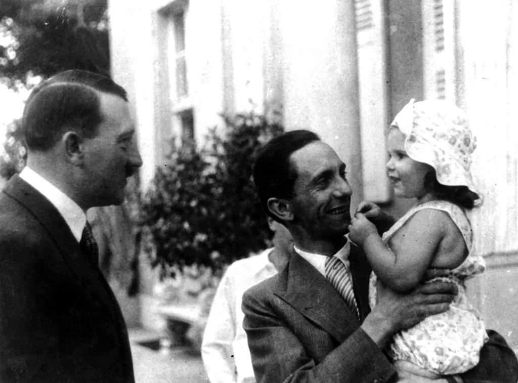 #40 German Chancellor Adolf Hitler, left, chats to his Propaganda Minister Dr, Goebbels who is holding his daughter Helga, during Hitler+s visit to their home in Berlin, 1934