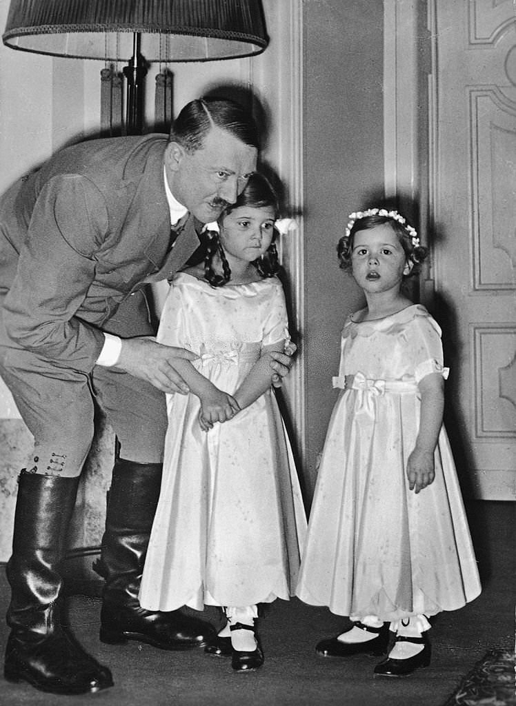 #56 Adolf Hitler adjusts the arms of one of Joseph Goebbels’ daughters as they and another Goebbels daughter pose for a photograph, late 1930s.