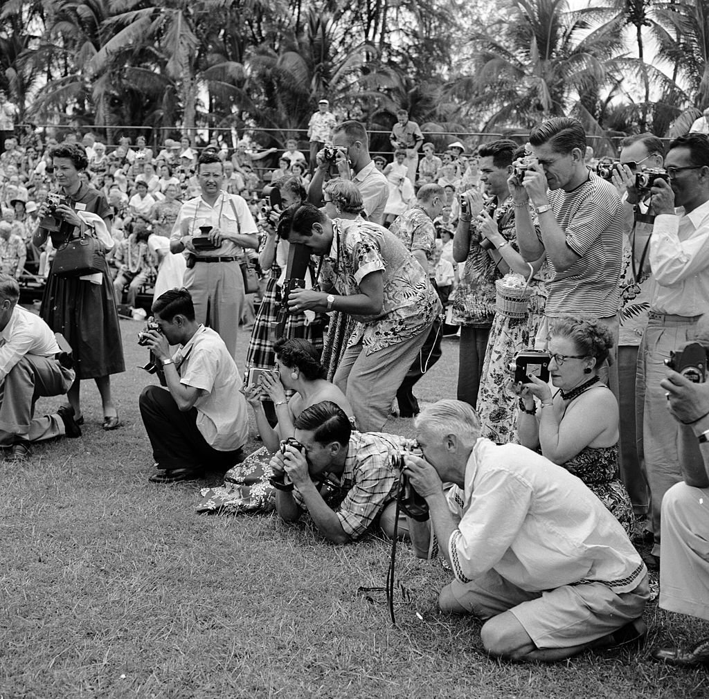 #134 A group of tourists, poised with cameras at the ready for the arrival of the Hula dancers on Honolulu’s Waikiki Beach, in Hawaii, 1953