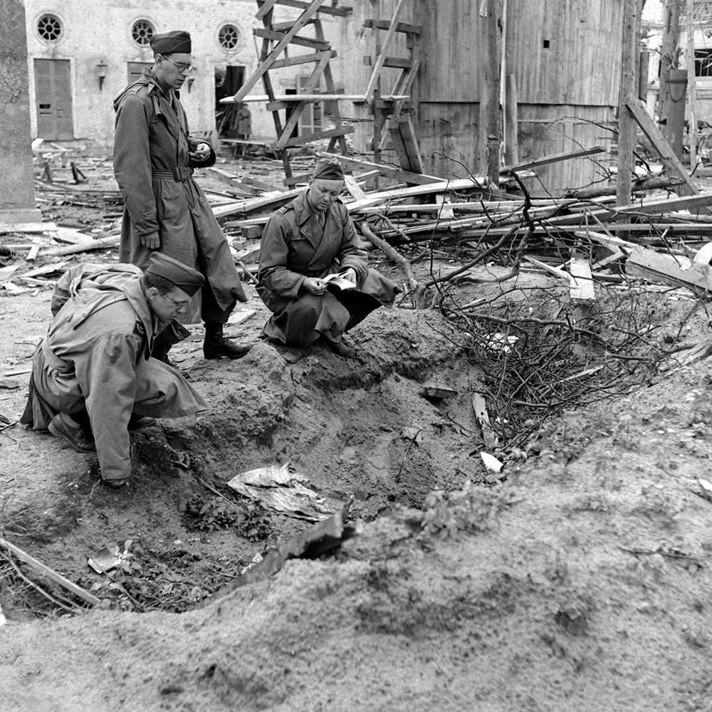 #11 LIFE correspondent Percy Knauth, left, sifts through debris in the shallow trench in the garden of the Reich Chancellery where, Knauth was told, the bodies of Hitler and Eva Braun were burned after their suicides.