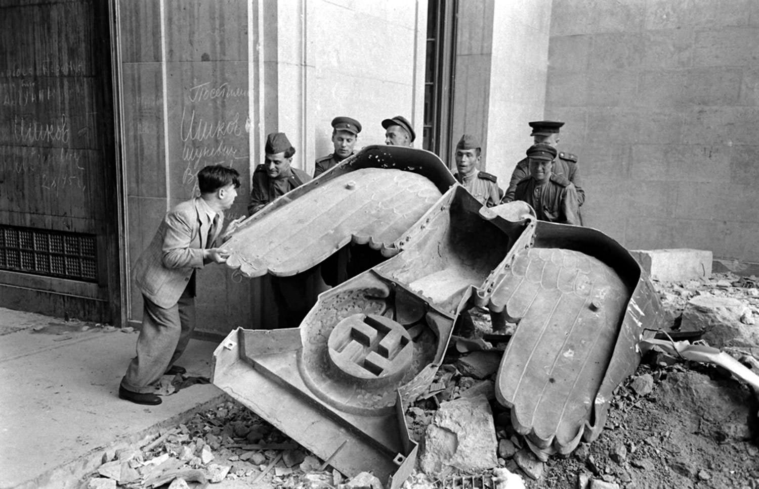 #16 Russian soldiers and a civilian struggle to move a large bronze Nazi Party eagle that once loomed over a doorway of the Reich Chancellery, Berlin, 1945.