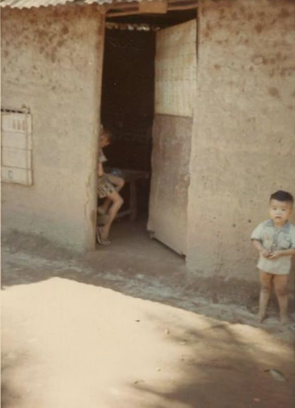 #27 The entrance to an unidentified Vietnamese house with a toddler boy standing outside, somewhere in South Vietnam during the Vietnam War