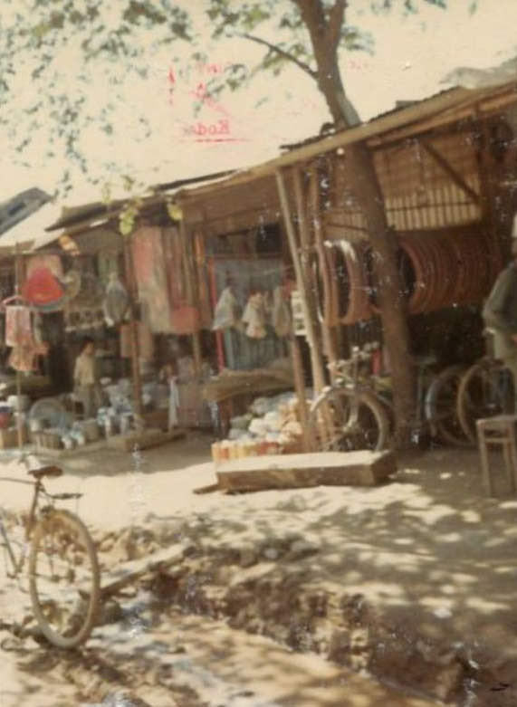 #6 A sidewalk scene with stores, including a bicycle shop, in a Vietnamese market in the city of Bồng Sơn in South Vietnam.