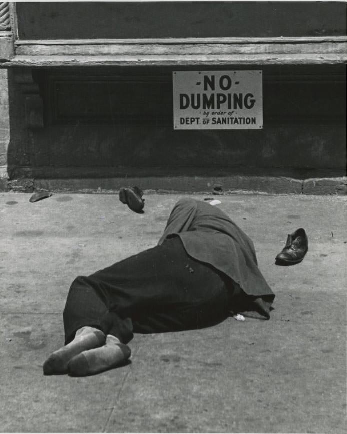 #15 A man sleeps on the ground under a sign that reads NO DUMPING by order of Dept. of Sanitation on the Lower East Side.