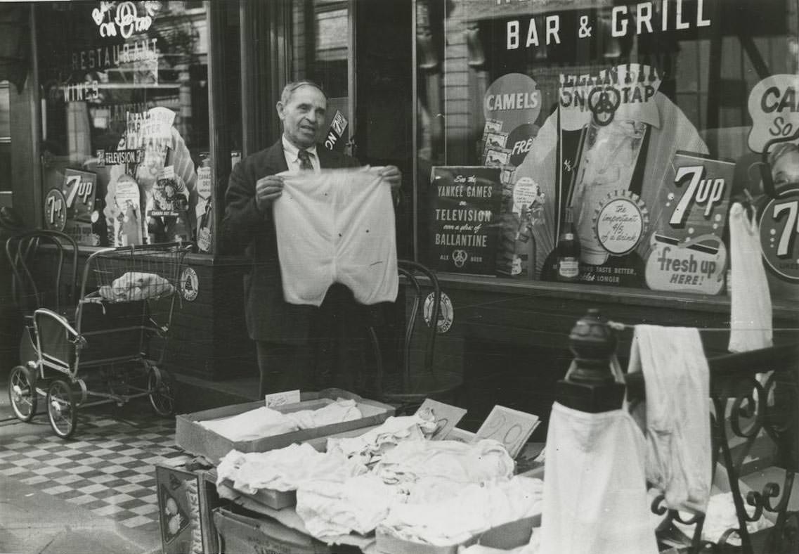 #20 A sidewalk merchant sells clothing in front of a bar and restaurant on the Lower East Side, 1948