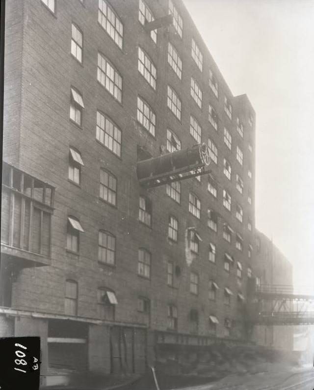 #81 A large piece of equipment is being manoeuvred out of building onto railway car below, 1924