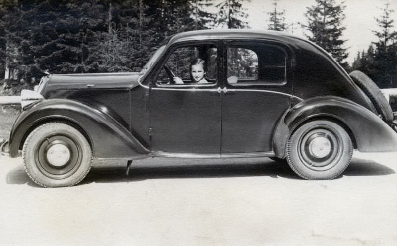 A young girl posing in the driver’s seat of a Steyr 100 on a country road in midday sunshine, 1938