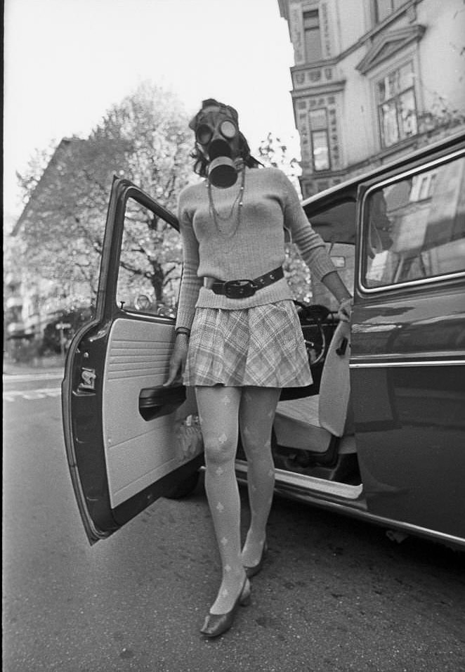 #256 Air pollution, young woman wearing a gas mask stepping out of her car, 1970