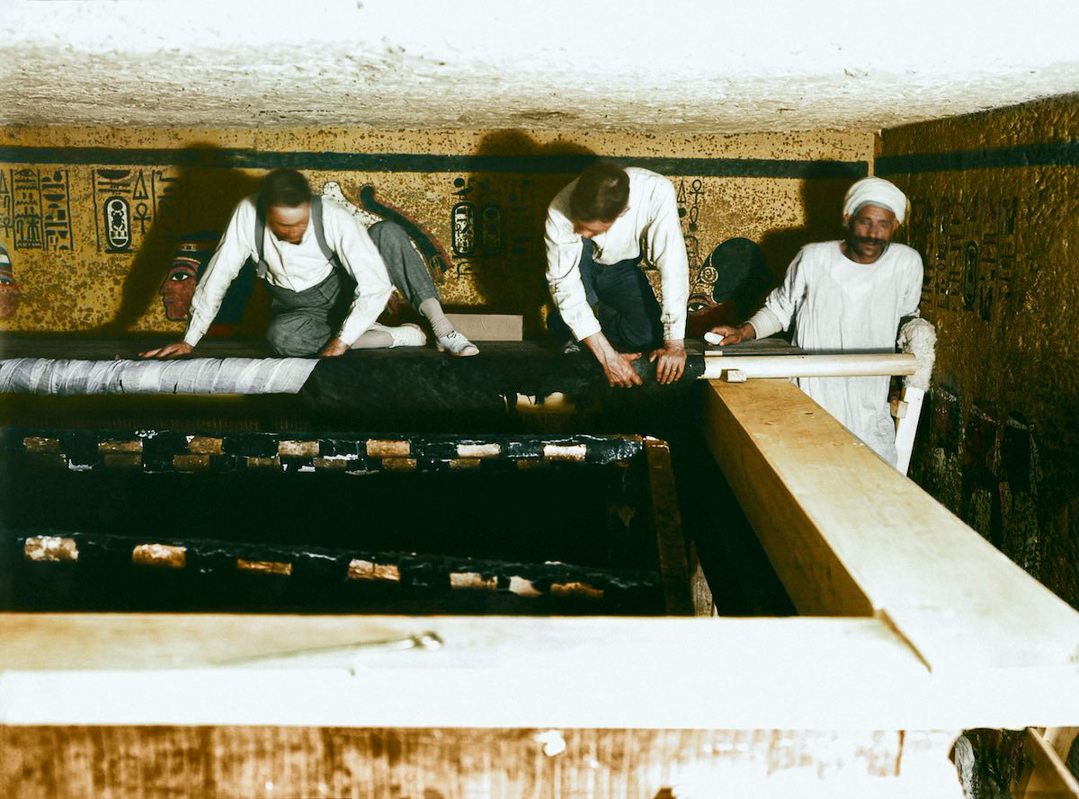 Howard Carter (left), Arthur Mace and an Egyptian workman standing on scaffolding, roll back the linen pall (Carter no. 209). Tutankhamun’s Tomb, 30th December 1923