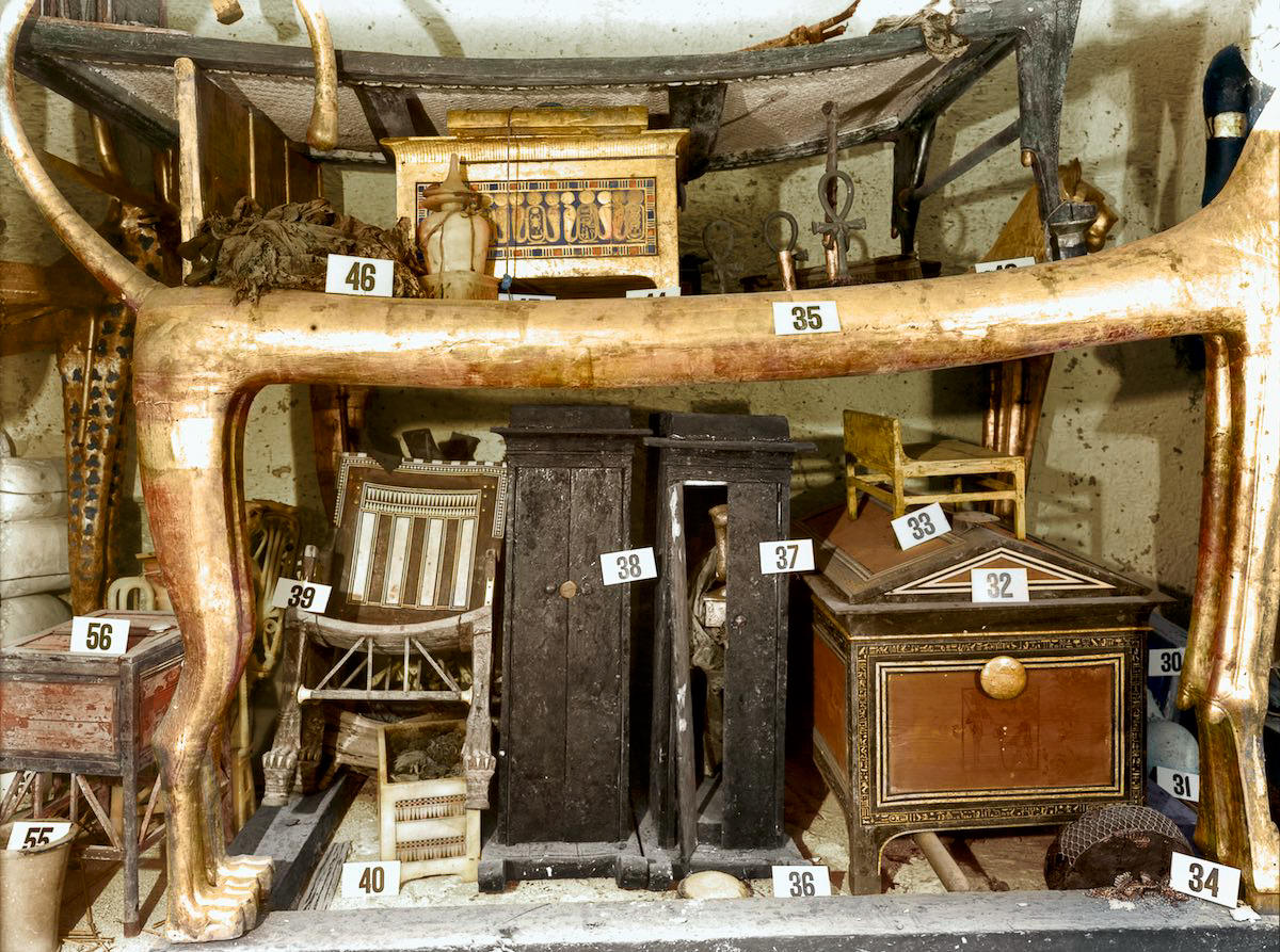 Objects stacked under the lion couch (Carter no. 35) against the west wall of the Antechamber. Tutankhamun’s Tomb, December 1925