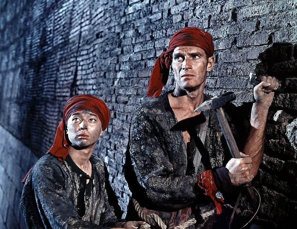 Charlton Heston chiseling at wall in a scene from the film ’55 Days At Peking’, 1963.