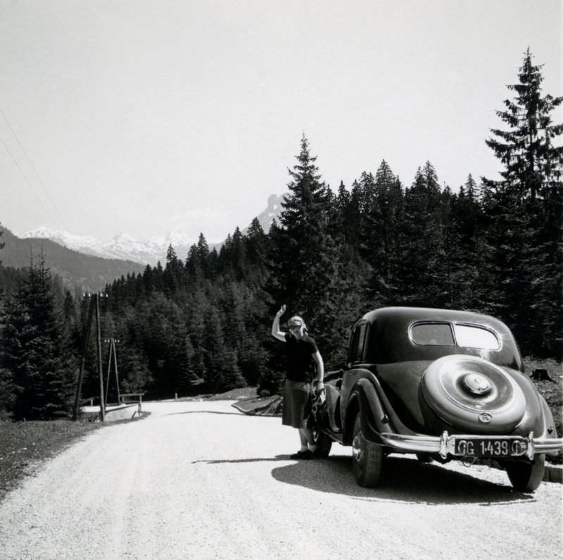 #27 A blonde lady posing next to a pre-war BMW 326 on an Alpine road, 1950.