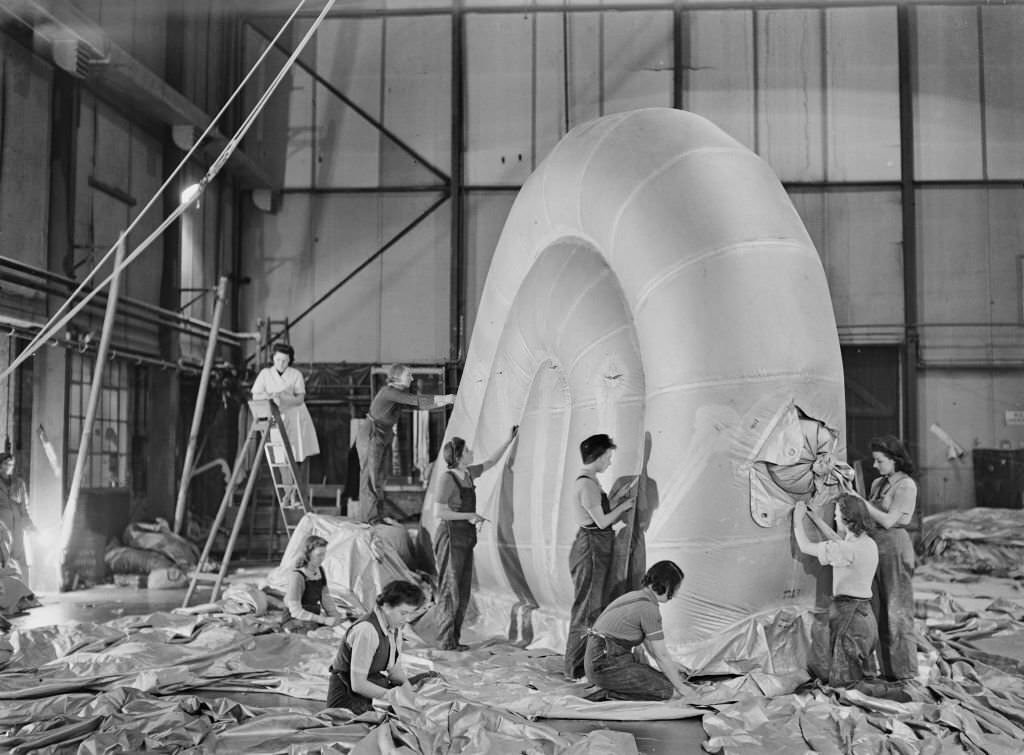 #106 Female workers, including a number wearing dungaree overalls, construct and assemble the fin of a barrage balloon in a factory hanger in England during World War II on 2nd December 1942.
