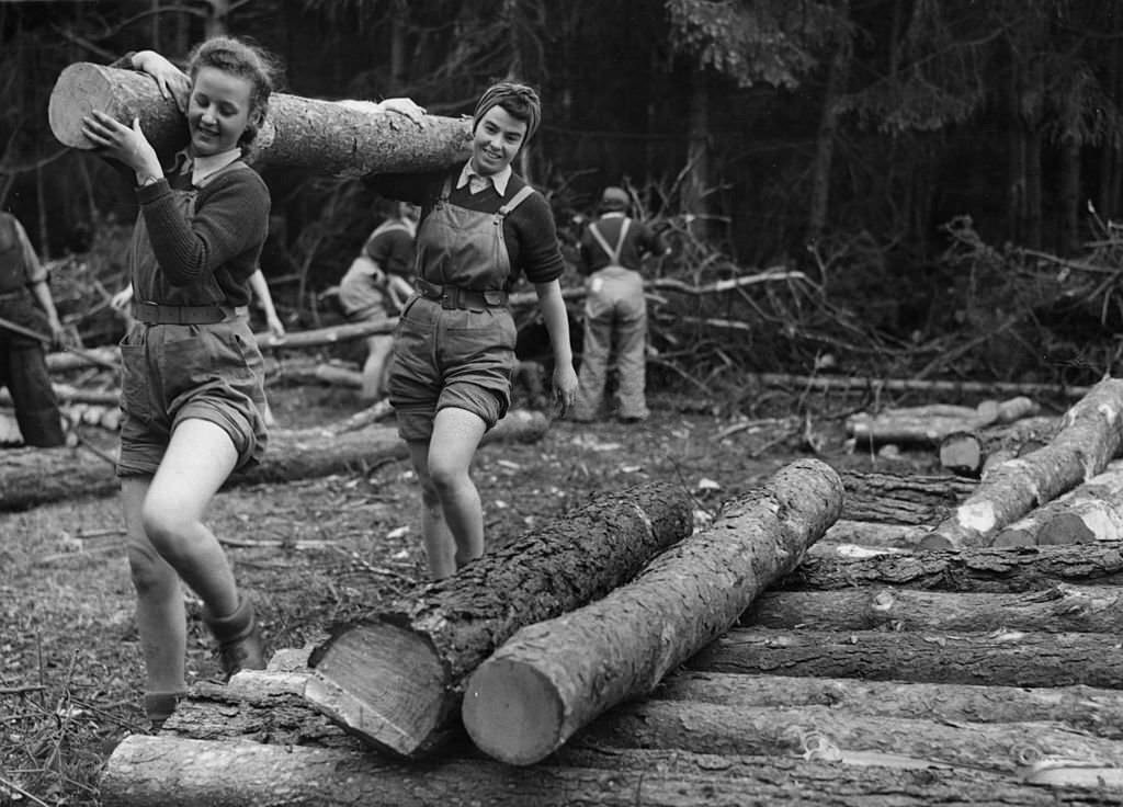 #116 Two members of the Women’s Timber Corps do their bit for the war effort by carrying a felled log through the lumber camp at Bury St Edmunds, Suffolk.