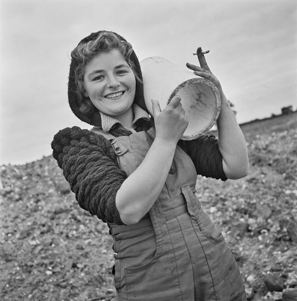 #137 Mrs Peggy Devine, an evacuee from London, holds a section of pipe as she carries out rough navvying work on the site of a new aerodrome being constructed in East Anglia during World War II on 16th September 1941.