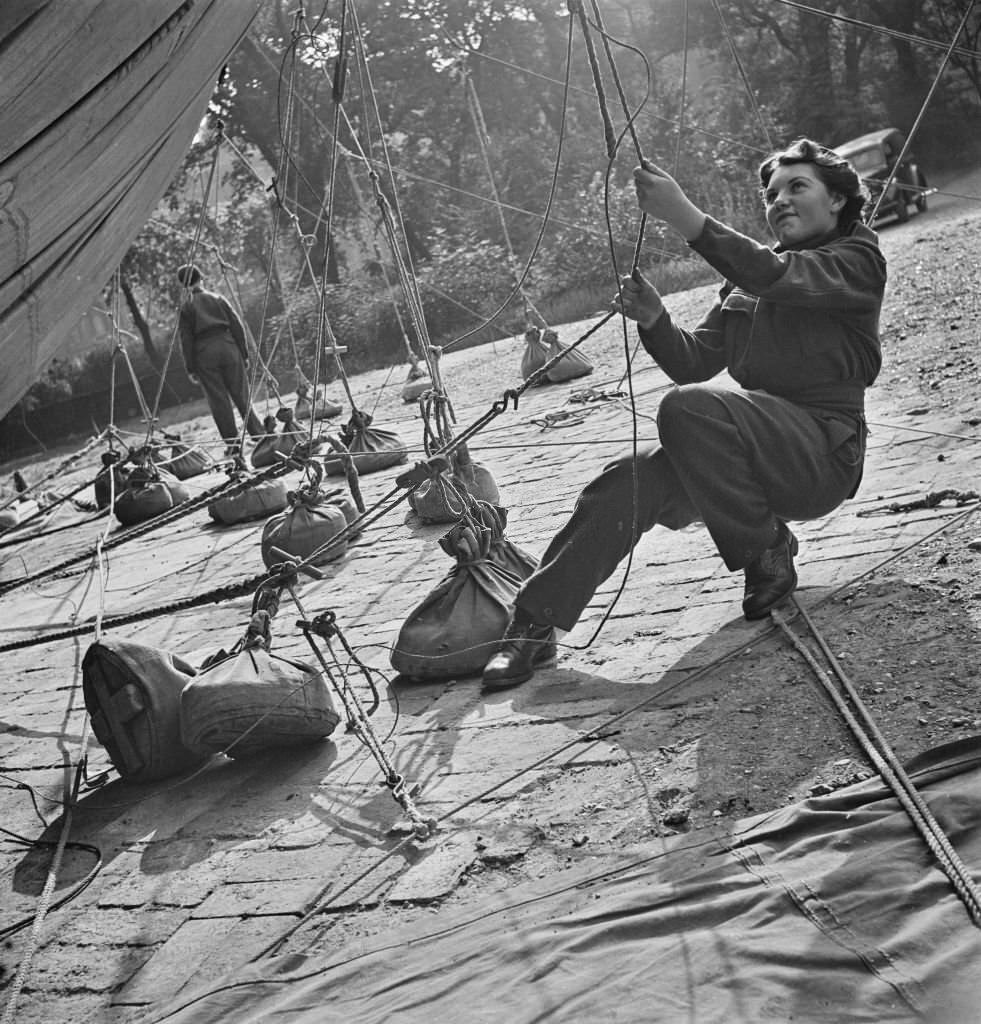 #142 A member of the Women’s Royal Air Force (WRAF) pulls on a rope to tighten up lines to a barrage balloon tethered in Grosvenor Gardens, London, September 1941.