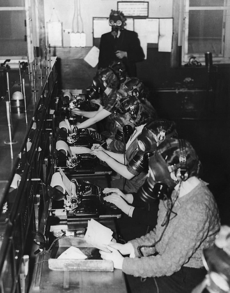 #153 Teleprinter telephone operators at work during a 15-minute gasmask drill, Scotland, 24th April 1941.