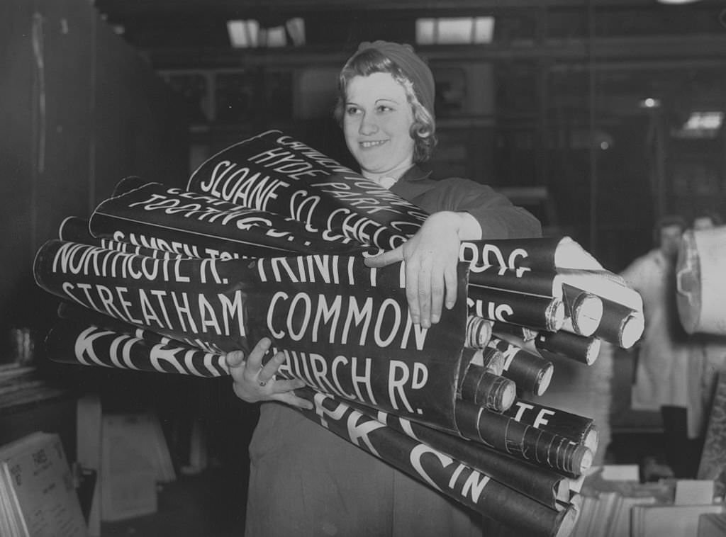 #163 Woman war worker E Oakham, carrying bus destination signs at the London Passenger Transport Board, 1941