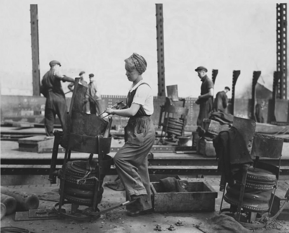 #45 A woman heating a rivet on a ship under construction. Women have entered previously male job fields in England during wartime, specifically shipbuilding.