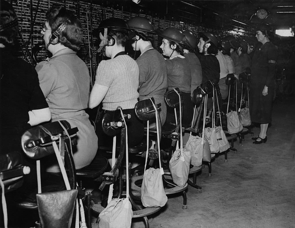 #73 Staff at work at a major London telephone exchange wearing tin helmets during an alert.