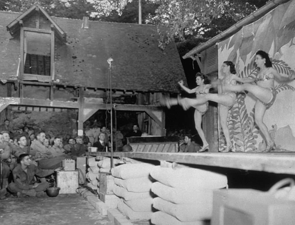 #79 A trio of French girls dance the can-can for GI’s in the rear echelon of an infantry unit in France, 1944