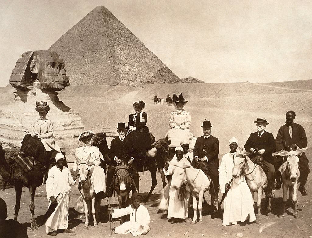#22 Edwardian tourists riding on donkeys and camels with their local guides at the Sphinx with a pyramid in the background at Giza, Egypt, 1910.
