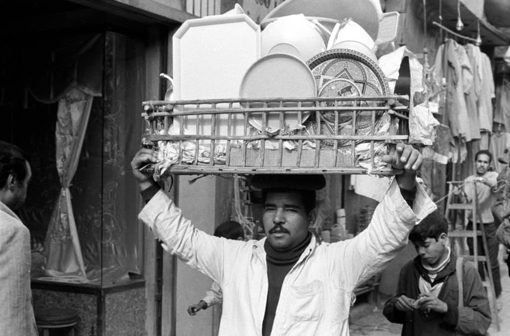 #42 A vendor carries a basket of household goods on his head at a bazaar in Cairo, 1972